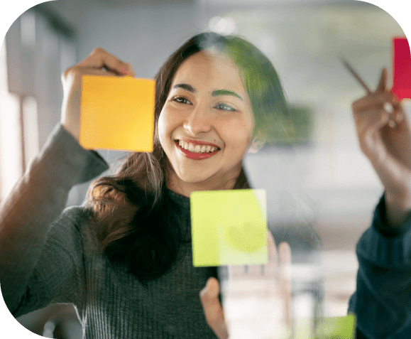 GettyImages-1460224745 (1) Smiling woman placing sticky notes on glass.